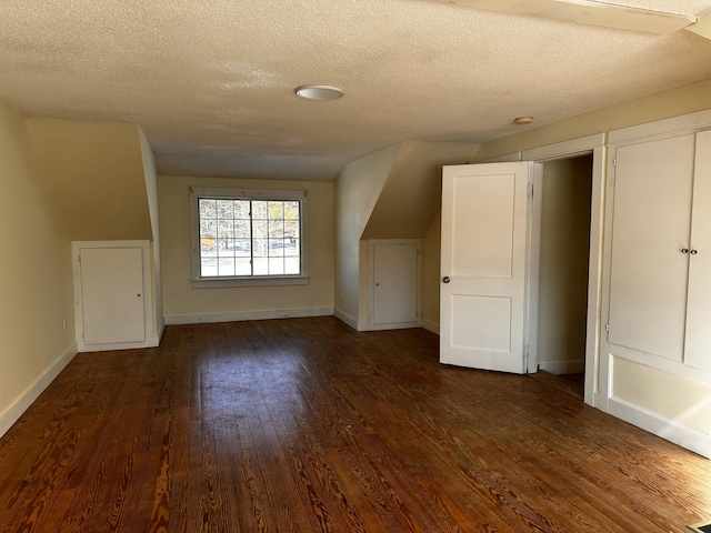 additional living space featuring a textured ceiling, lofted ceiling, and dark wood-type flooring