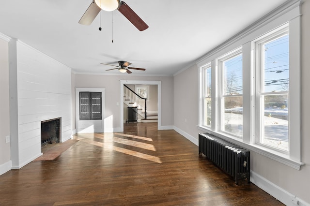 unfurnished living room featuring radiator, a large fireplace, ceiling fan, dark wood-type flooring, and crown molding