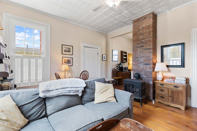 living room with ceiling fan, light hardwood / wood-style floors, a wood stove, and ornamental molding