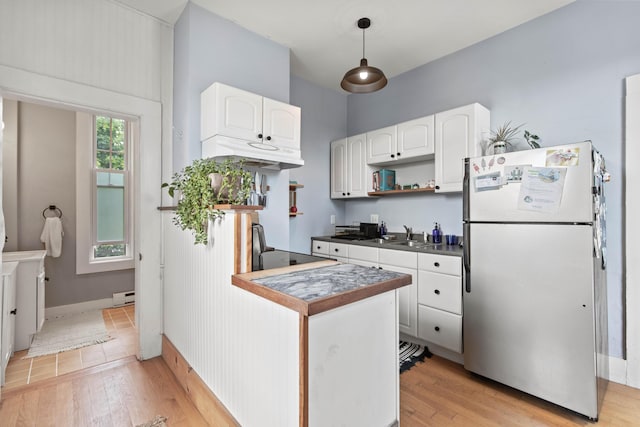 kitchen featuring stainless steel refrigerator, white cabinetry, hanging light fixtures, and a baseboard heating unit