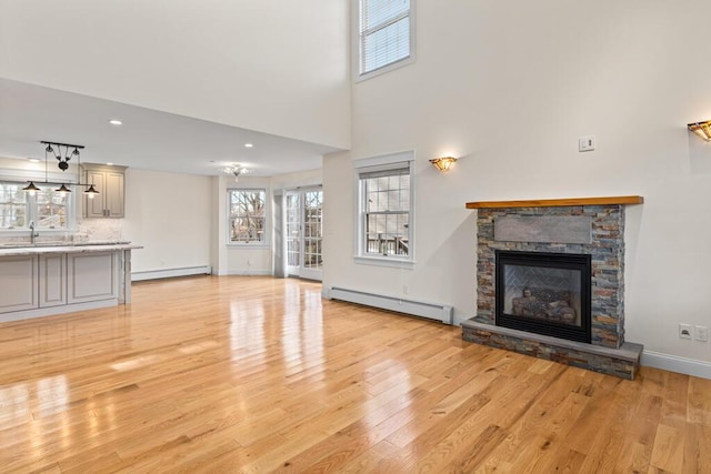 unfurnished living room with light wood-type flooring, a stone fireplace, baseboard heating, and sink