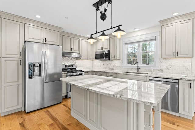 kitchen featuring appliances with stainless steel finishes, tasteful backsplash, sink, light hardwood / wood-style flooring, and a center island