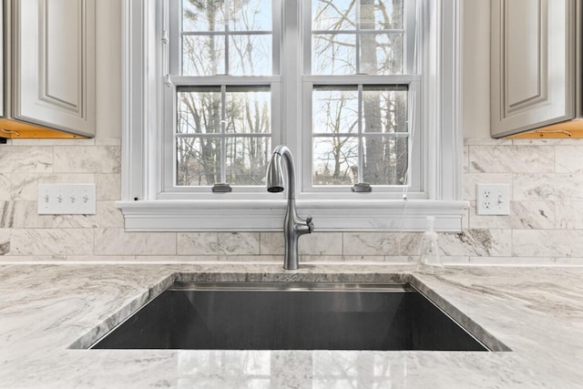 interior details with gray cabinets, light stone counters, and sink