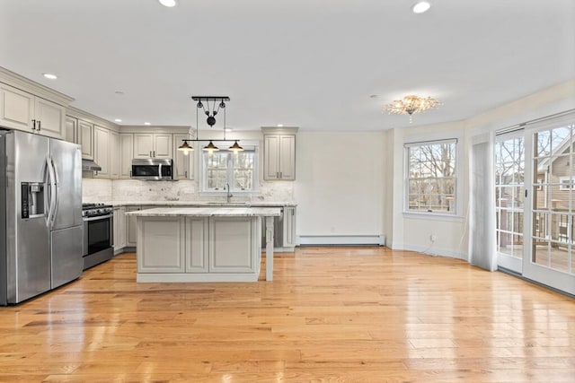 kitchen with stainless steel appliances, baseboard heating, backsplash, decorative light fixtures, and a kitchen island