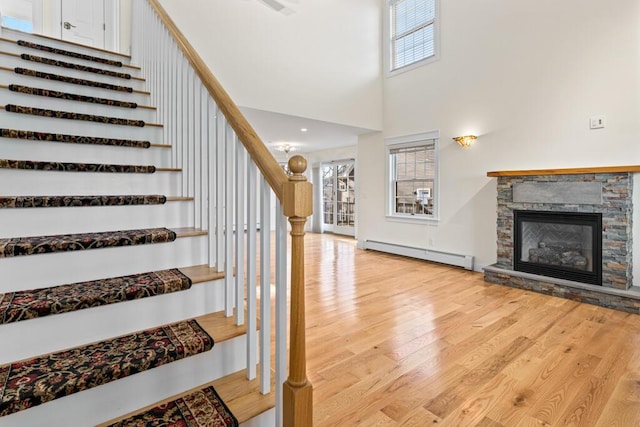 stairs featuring a stone fireplace, a healthy amount of sunlight, a baseboard radiator, and wood-type flooring