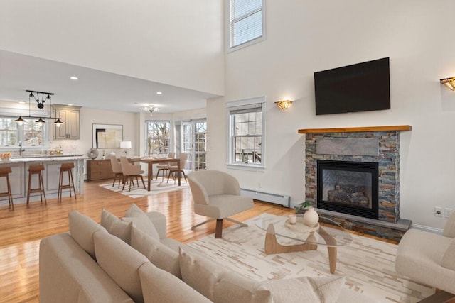 living room with sink, a baseboard radiator, a towering ceiling, a fireplace, and light wood-type flooring