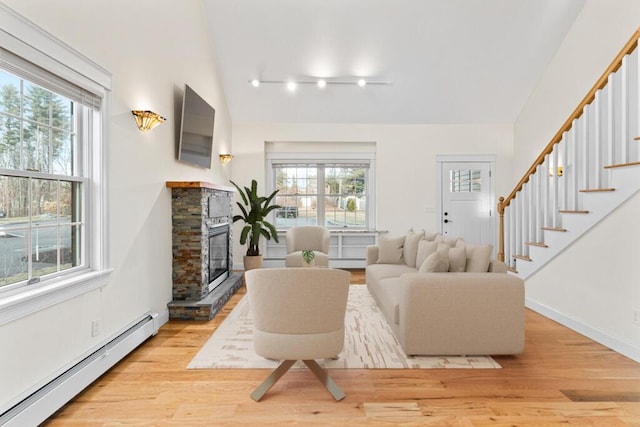 living room featuring vaulted ceiling, a stone fireplace, light hardwood / wood-style flooring, and a baseboard radiator