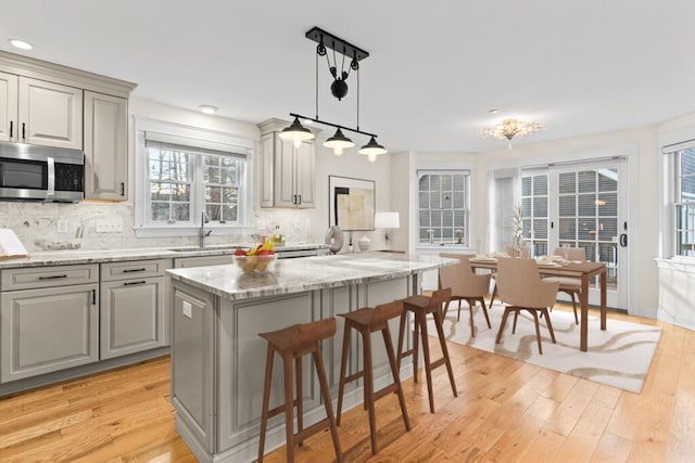 kitchen with a center island, sink, hanging light fixtures, light stone counters, and decorative backsplash