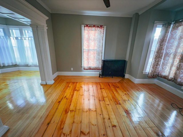 unfurnished room with light hardwood / wood-style floors, ornamental molding, radiator, and ornate columns