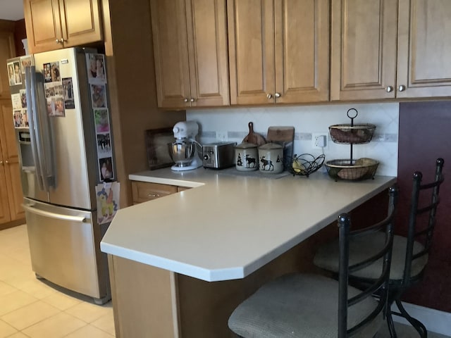 kitchen with a kitchen breakfast bar, stainless steel fridge, kitchen peninsula, and light tile patterned floors