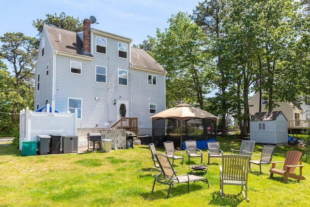 back of house featuring a gazebo, a storage unit, an outdoor fire pit, and a lawn