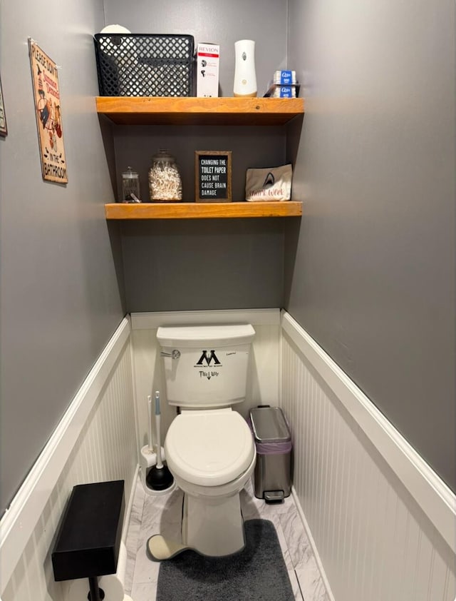 bathroom with toilet, marble finish floor, and a wainscoted wall