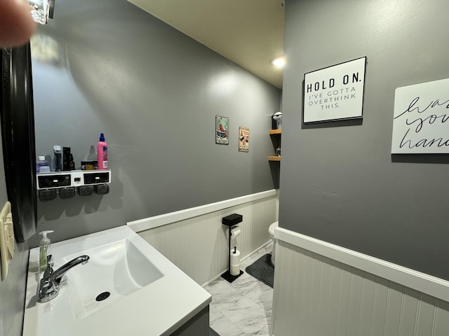 bathroom featuring marble finish floor, wainscoting, and a sink