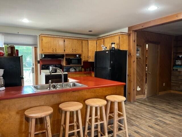 kitchen with white range with electric cooktop, black refrigerator, light hardwood / wood-style flooring, a kitchen bar, and kitchen peninsula