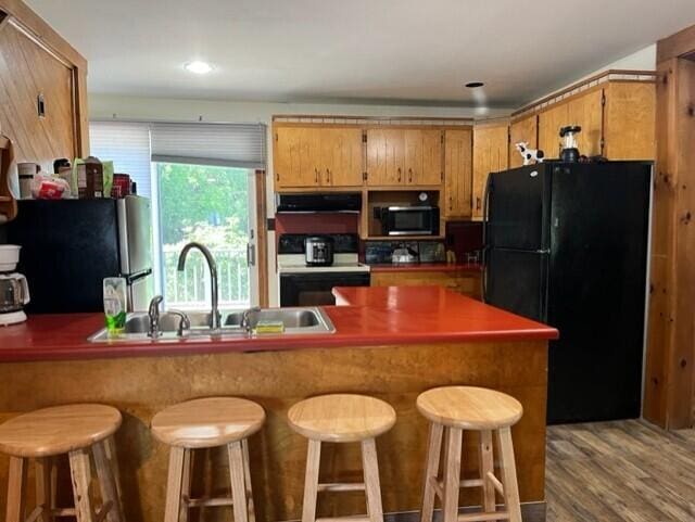 kitchen featuring sink, white range with electric stovetop, stainless steel fridge, a breakfast bar area, and black refrigerator