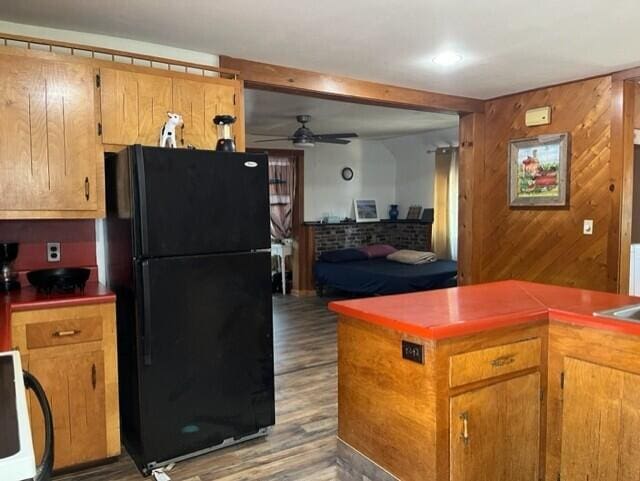 kitchen with ceiling fan, black refrigerator, wood-type flooring, and wooden walls