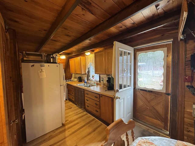 kitchen with sink, wooden walls, light wood-type flooring, white fridge, and beam ceiling