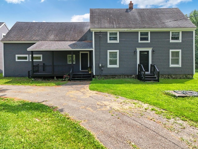 colonial-style house with covered porch, a front lawn, a chimney, and a shingled roof