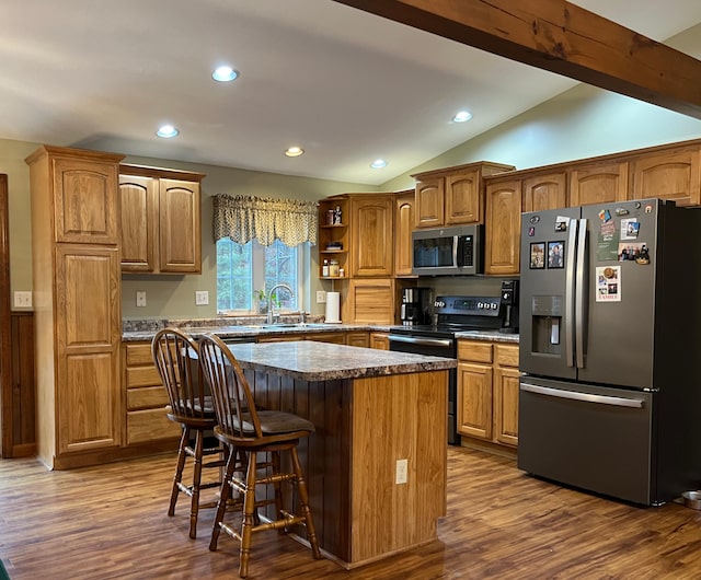 kitchen with vaulted ceiling with beams, a kitchen island, a kitchen bar, wood-type flooring, and stainless steel appliances