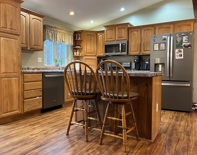 kitchen featuring a kitchen bar, appliances with stainless steel finishes, hardwood / wood-style flooring, and vaulted ceiling