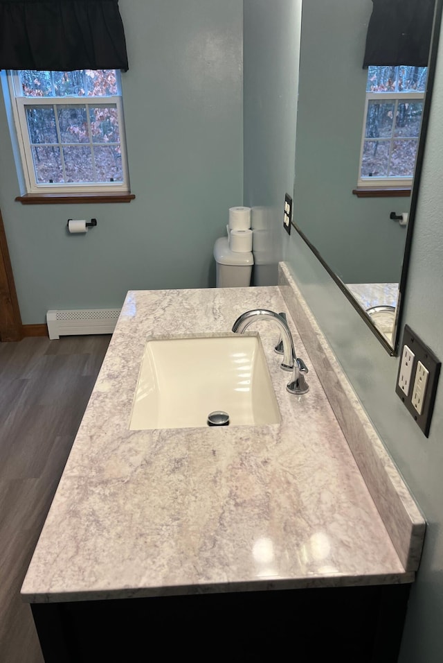 bathroom featuring vanity, toilet, wood-type flooring, and a baseboard heating unit