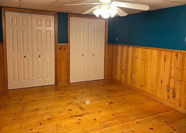 unfurnished bedroom with a paneled ceiling, ceiling fan, multiple closets, and light hardwood / wood-style flooring