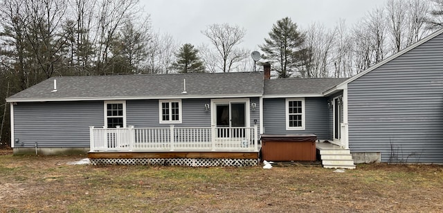 back of property featuring a lawn, a wooden deck, and a hot tub