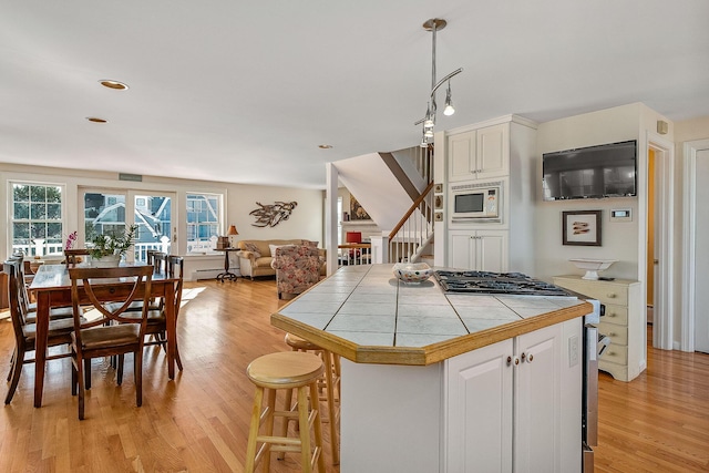 kitchen featuring hanging light fixtures, white cabinets, tile countertops, a kitchen bar, and white microwave