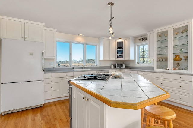 kitchen featuring white fridge, white cabinetry, hanging light fixtures, and stainless steel gas range