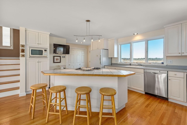 kitchen featuring tile countertops, white appliances, sink, hanging light fixtures, and white cabinetry