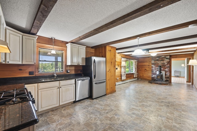 kitchen with a wood stove, sink, stainless steel appliances, beamed ceiling, and wood walls