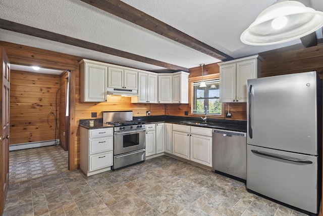 kitchen with pendant lighting, wood walls, sink, appliances with stainless steel finishes, and beamed ceiling