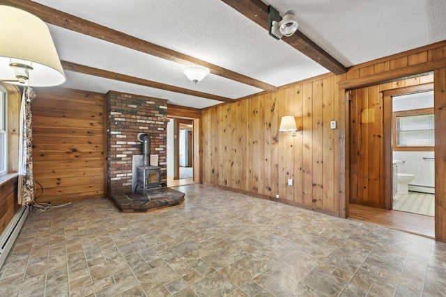 unfurnished living room with beam ceiling, a wood stove, wood walls, and a textured ceiling