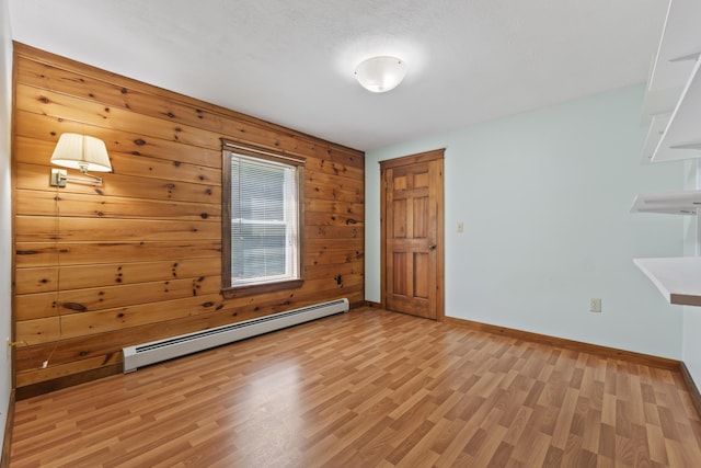 empty room with wooden walls, a baseboard radiator, a textured ceiling, and light hardwood / wood-style floors