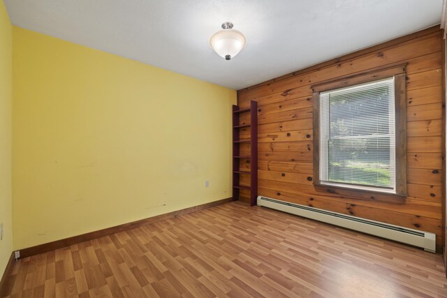 spare room featuring light hardwood / wood-style floors, baseboard heating, and wooden walls