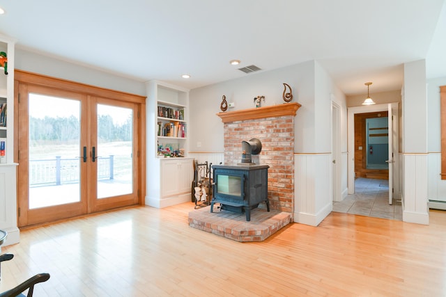 living room featuring light hardwood / wood-style flooring, french doors, a wood stove, built in shelves, and a baseboard radiator