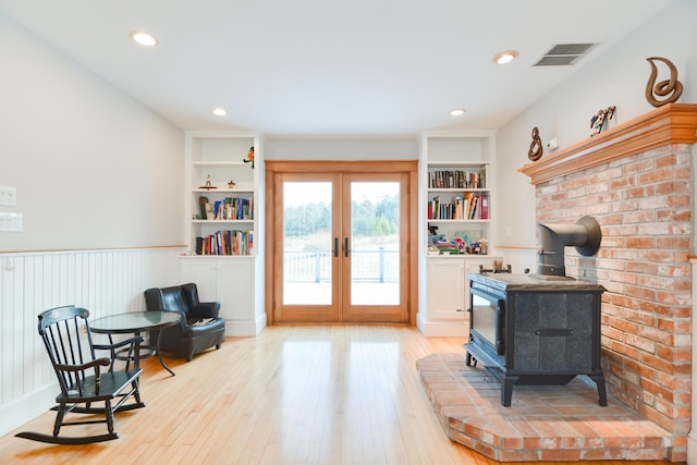 interior space with light hardwood / wood-style floors, french doors, built in features, and a wood stove