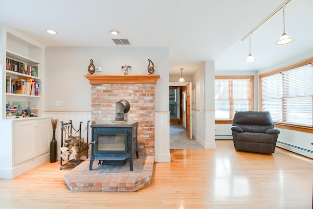 living room with built in shelves, baseboard heating, a wood stove, and light wood-type flooring