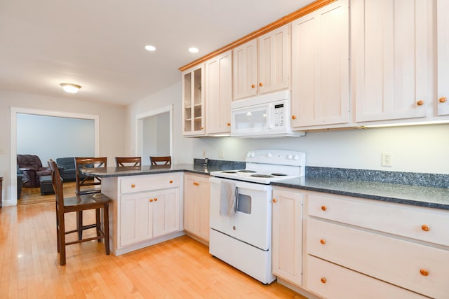 kitchen with white appliances, kitchen peninsula, light hardwood / wood-style floors, a breakfast bar area, and white cabinets