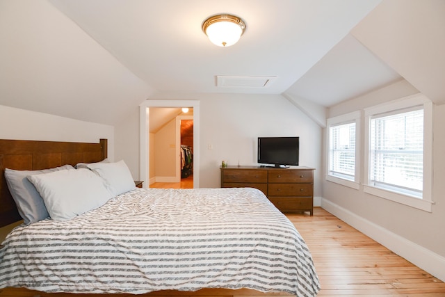 bedroom featuring a spacious closet, light wood-type flooring, a closet, and lofted ceiling