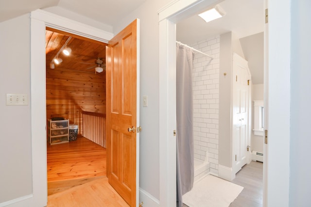 hallway with light wood-type flooring, a baseboard radiator, and lofted ceiling