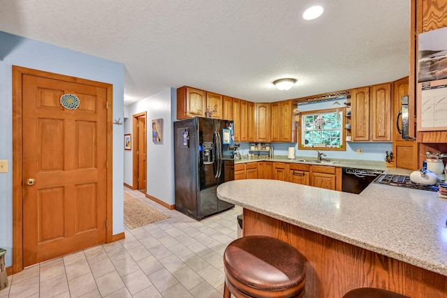 kitchen with kitchen peninsula, a breakfast bar, a textured ceiling, sink, and black appliances