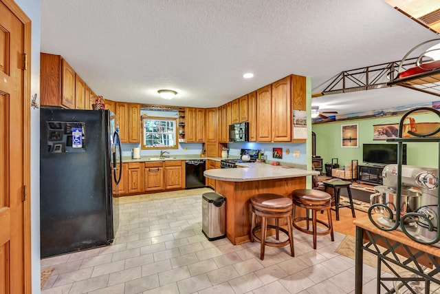 kitchen featuring a kitchen bar, light tile patterned floors, a textured ceiling, and black appliances