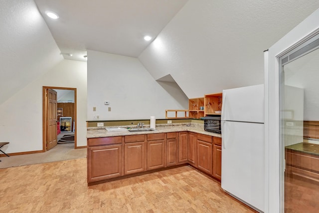 kitchen with light stone countertops, kitchen peninsula, sink, white fridge, and lofted ceiling