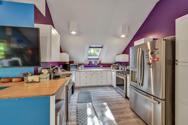 kitchen featuring light wood-type flooring, stainless steel appliances, white cabinetry, and vaulted ceiling with skylight