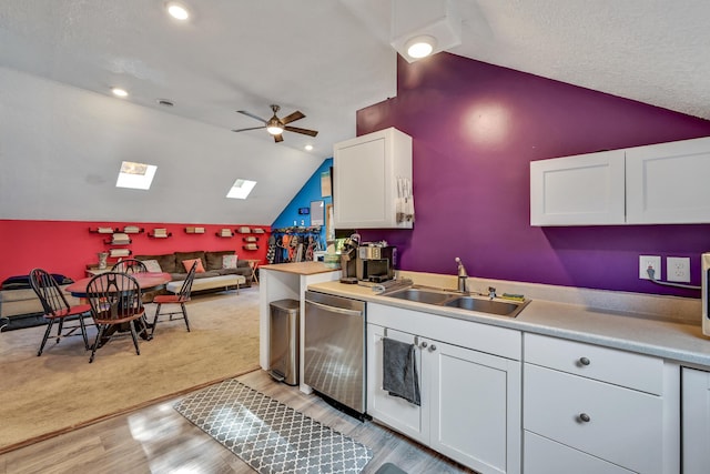 kitchen with dishwasher, white cabinets, sink, vaulted ceiling with skylight, and ceiling fan