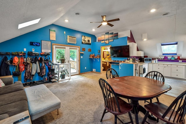 carpeted dining area featuring ceiling fan, french doors, a wall mounted air conditioner, lofted ceiling with skylight, and a textured ceiling