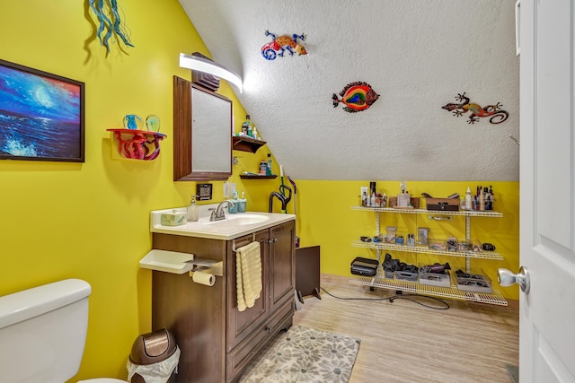 bathroom featuring hardwood / wood-style floors, vanity, lofted ceiling, toilet, and a textured ceiling