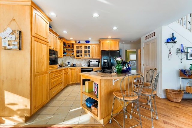 kitchen featuring a center island, tasteful backsplash, a kitchen bar, light tile patterned floors, and black appliances