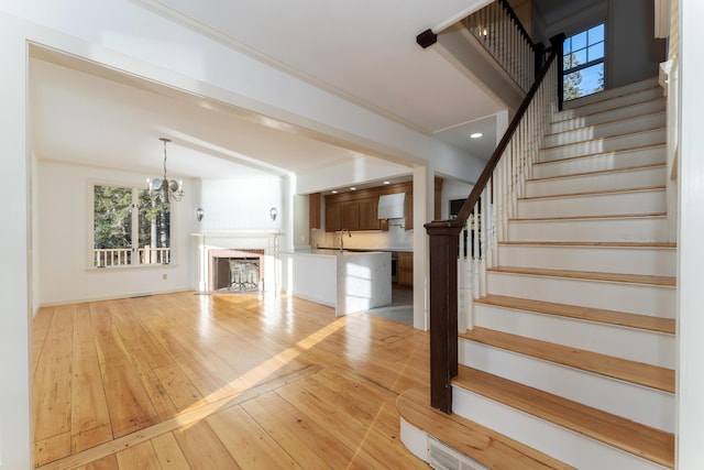 stairs with hardwood / wood-style floors, crown molding, sink, and a chandelier